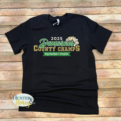 A black short sleeve t-shirt with a 3-color glitter design saying 2025 Damascus County Champs Division 1 Poms. It features a gold and white pom pom surrounding Damascus in script.