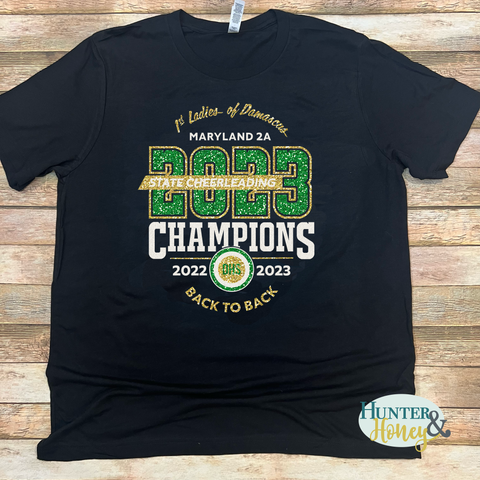 2023 Damascus Cheer MD 2A State Champs Intertwined t-shirt with a 3-color glitter logo (gold, white, and dark green) on a black t-shirt. 