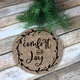 7" round natural cork trivet with black script Comfort and Joy graphic with a vine and berries laurel border.