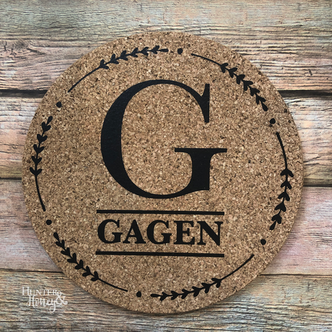 7" round natural cork customized trivet with a single large letter monogram and family last name under the letter surrounded by a leaf and dot border.
