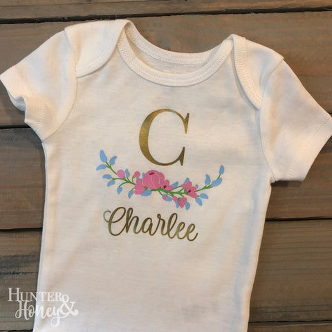 Infant bodysuit with large metallic gold initial, flowers, and full name.